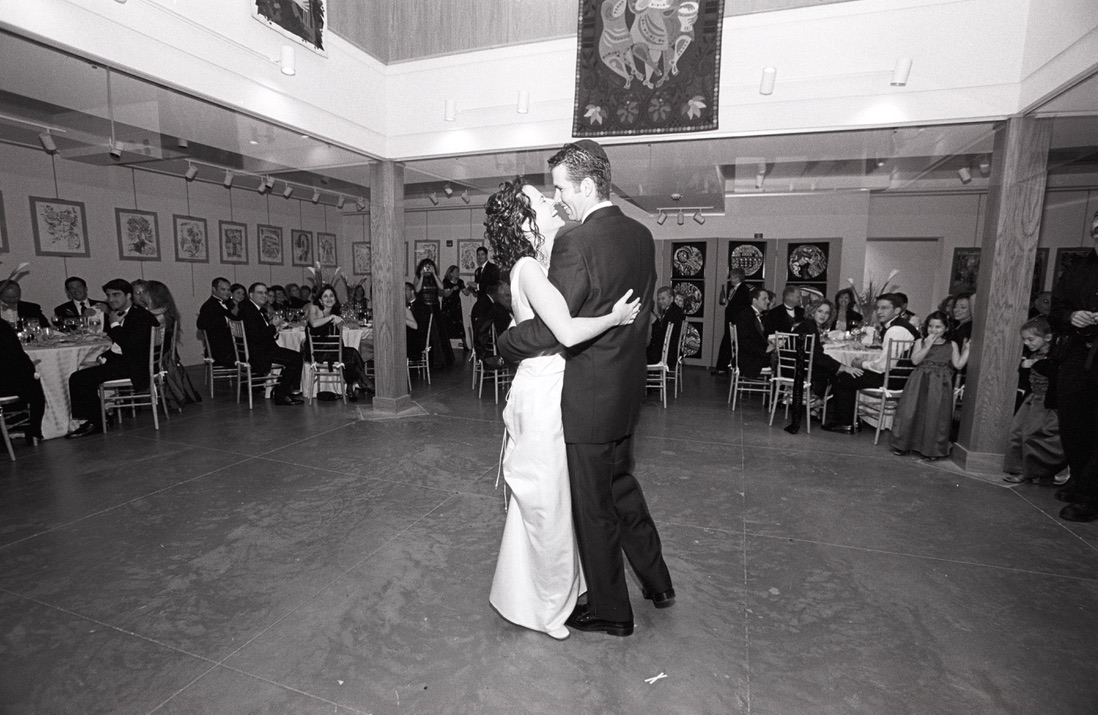 A couple sharing their first dance in the Museum's gallery during their wedding reception, surrounded by guests and framed artwork